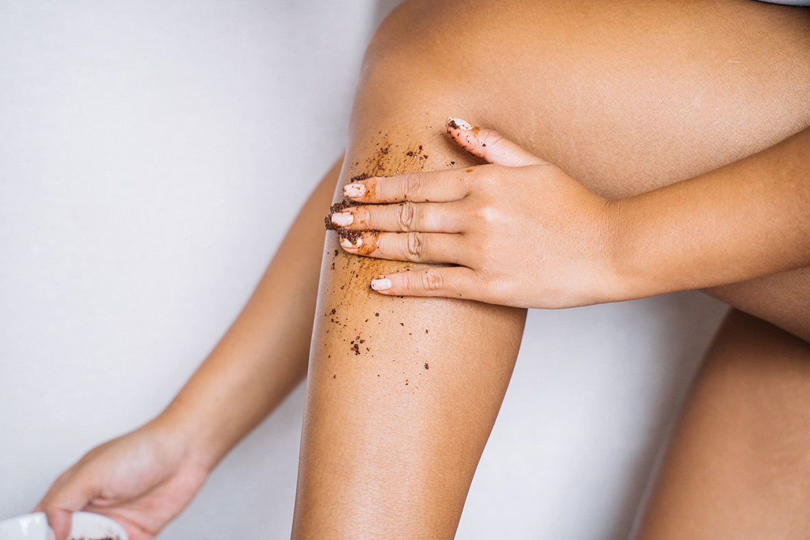 A woman applies exfoliating shower gel to her legs.